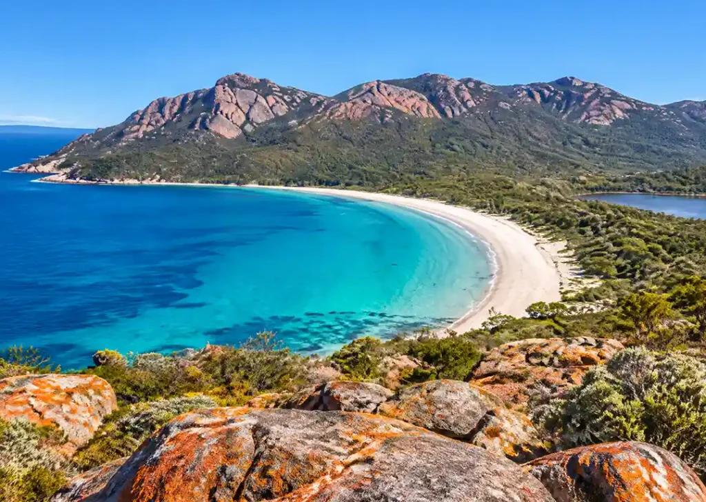 Elevated view of vibrant turquoise ocean water, white sand beach, and pink granite mountains on the East Coast of Tasmania