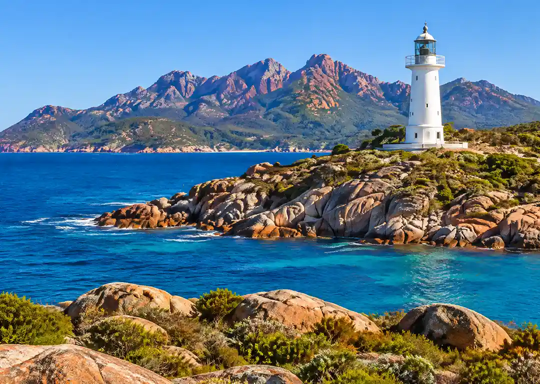 White Cape Tourville Lighthouse standing on granite cliffs overlooking turquoise ocean waters and The Hazards mountains in Freycinet National Park Tasmania