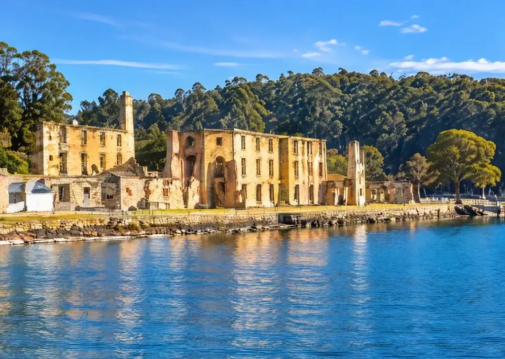 Historic sandstone penitentiary ruins of Port Arthur on the waterfront of Mason Cove surrounded by green hills in Tasmania